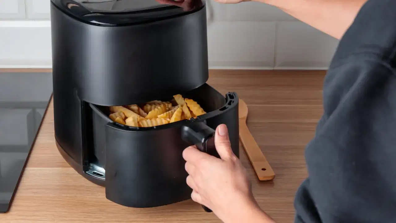 Ręka wyjmuje z frytkownicy beztłuszczowej koszyk z chrupiącymi frytkami. Czy pieczone frytki są zdrowe?