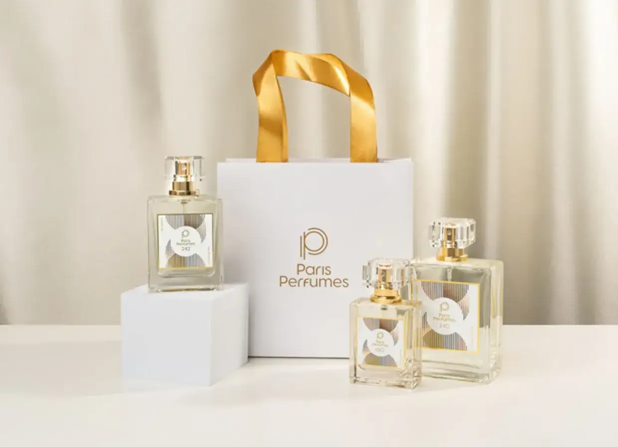 Eleganckie pamiątki z Paryża: trzy flakony perfum Paris Perfumes o różnych pojemnościach, obok białej torby z logo.