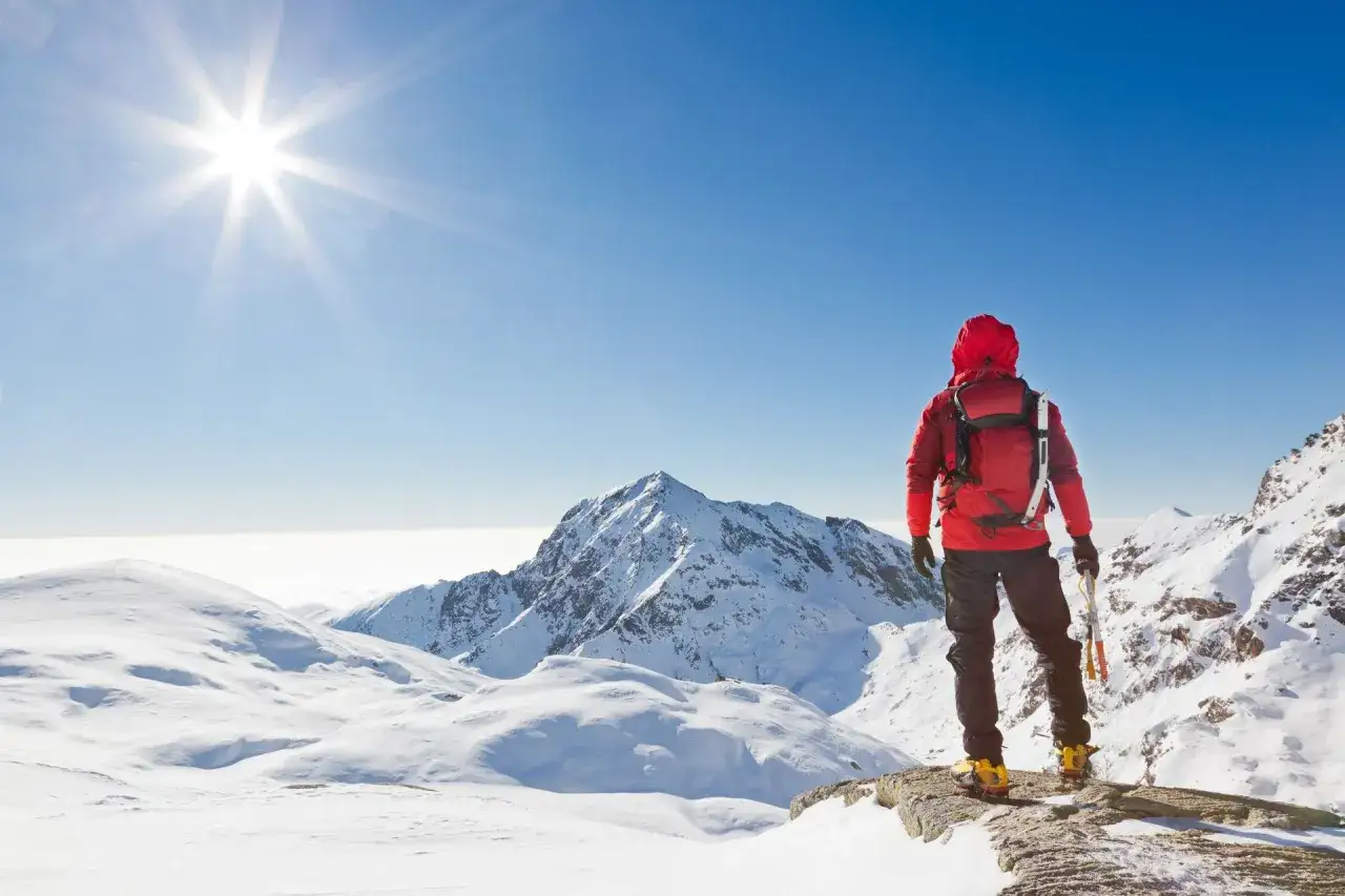 Alpinista w czerwonej kurtce na szczycie, podziwia widok. Słońce świeci jasno, a wok&oacute;ł śnieg. Może czuć pierwsze objawy choroby wysokościowej.
