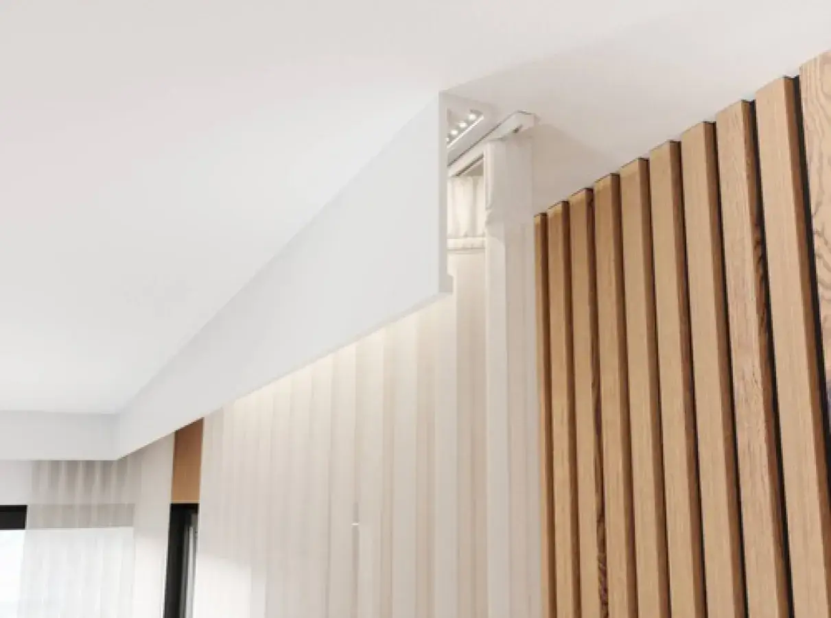 Nowoczesna listwa przysufitowa LED tworzy subtelne oświetlenie, podkreślając drewnianą ścianę i delikatne zasłony.
