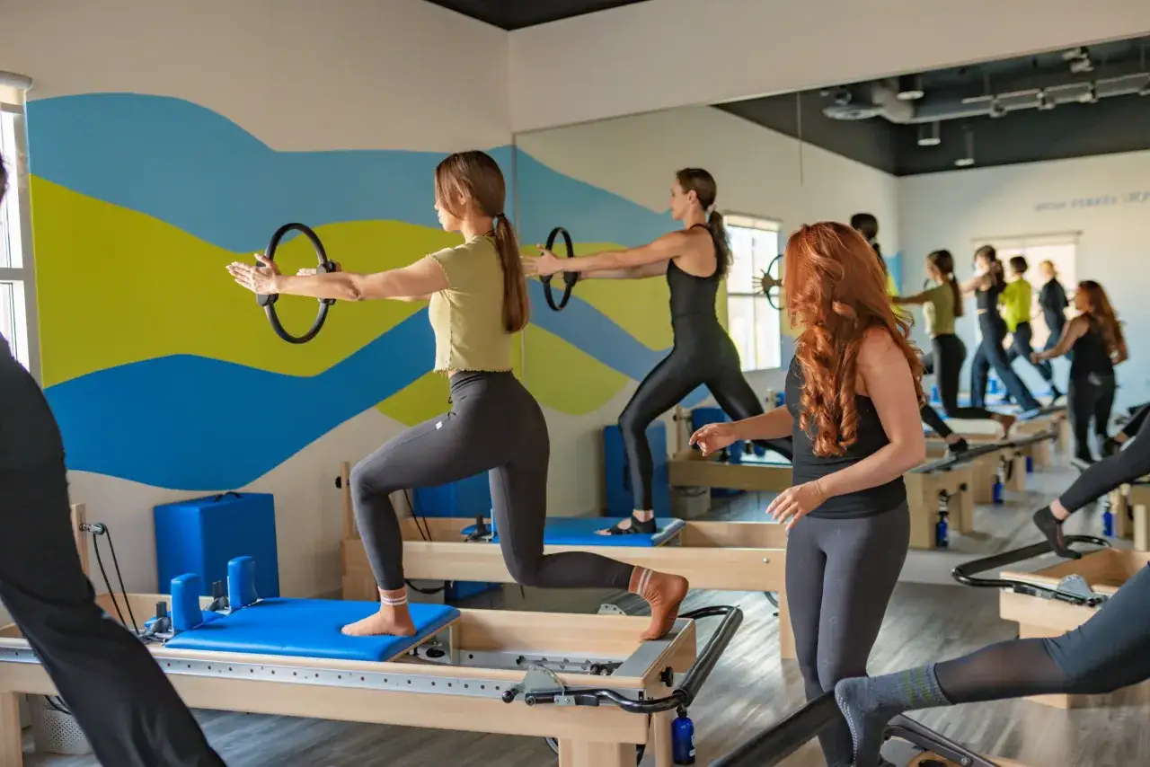 Kobiety ćwiczą na reformers, używając k&oacute;łka do pilates. Trening na tym stroju do pilates wzmacnia ciało.