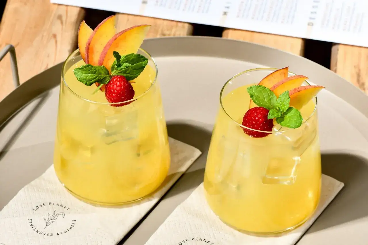 Dwa orzeźwiające, domowe drinki z martini, ozdobione brzoskwinią, maliną i miętą, idealne na letnie popołudnie.