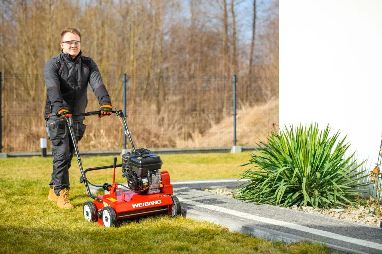 Mężczyzna w okularach i rękawicach obsługuje wertykulator Weidemann. Po wertykulacji trawnika warto zastosować odpowiedni nawóz.