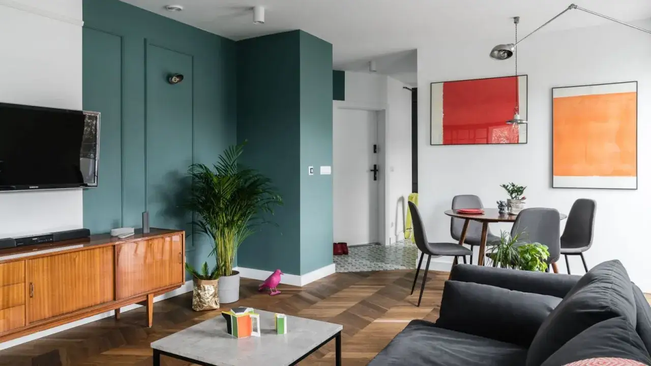 Nowoczesny salon z drewnianą podłogą i kolorowymi obrazami. Dowiedz się, jak powiesić obraz na ścianie, by stworzyć podobny efekt.