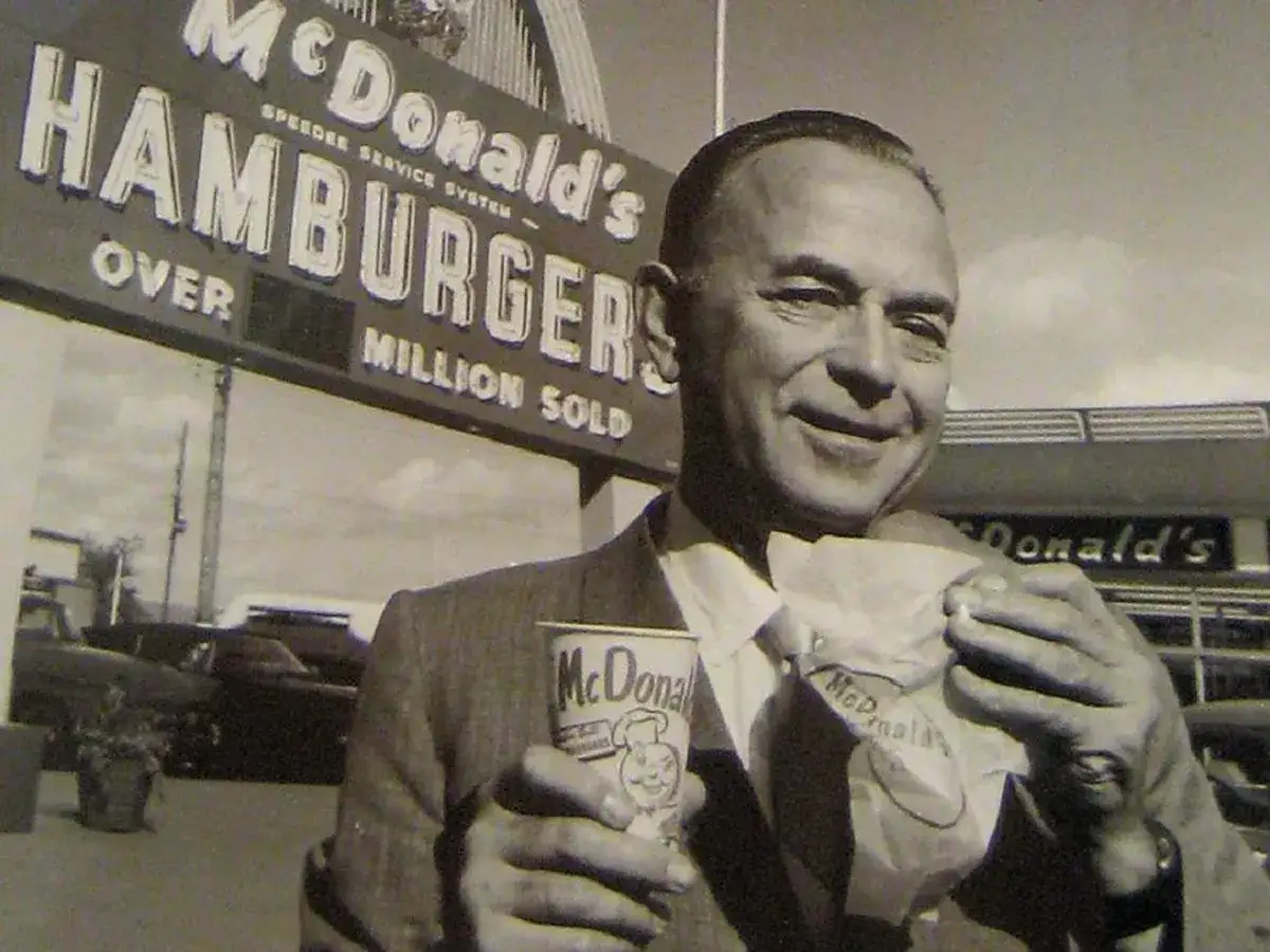 Ray Kroc, który wymyślił McDonald's, trzyma hamburgera i kubek z logo.