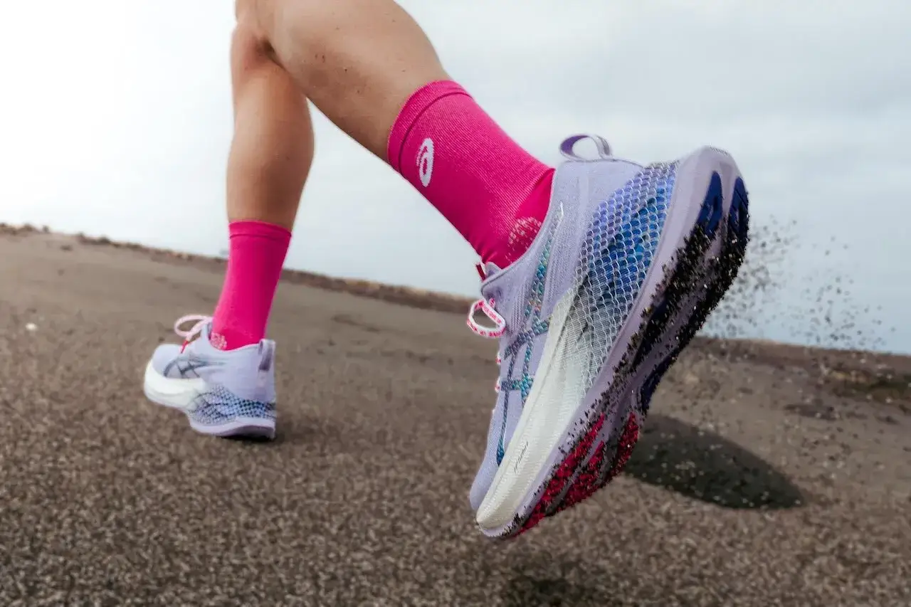 Lekkie, fioletowe buty na maraton z różowymi skarpetkami, w akcji na piaszczystym podłożu.