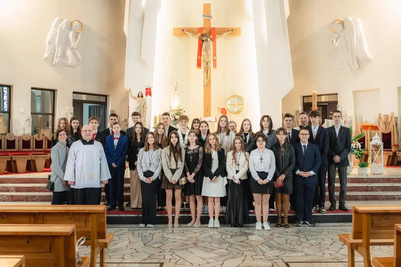 Młodzież w kościele, gotowa na bierzmowania. Uśmiechnięci młodzi ludzie pozują do pamiątkowego zdjęcia z kapłanem.