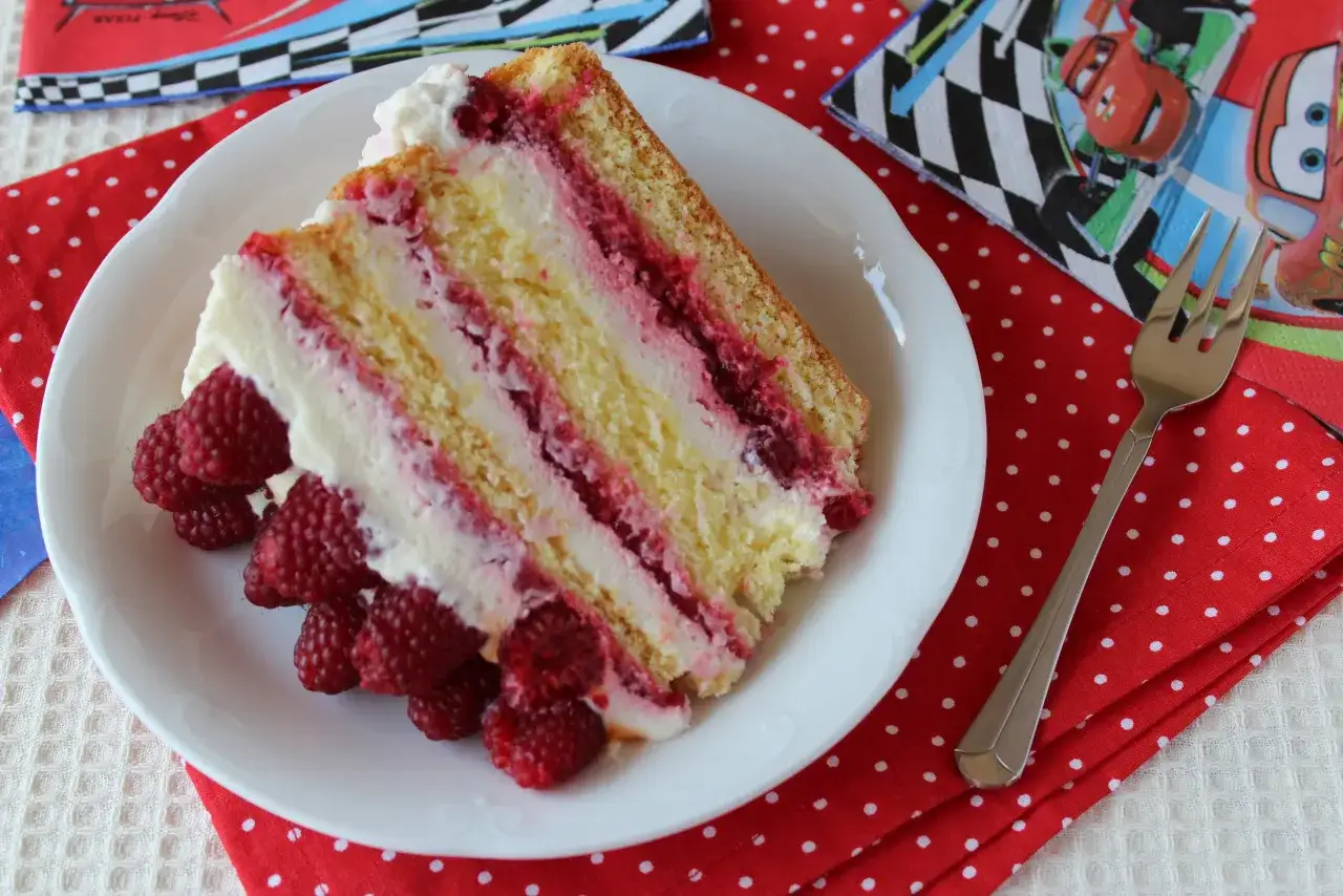 Pyszny tort śmietankowo-malinowy z mascarpone, udekorowany świeżymi malinami. Idealny na dziecięce przyjęcie.