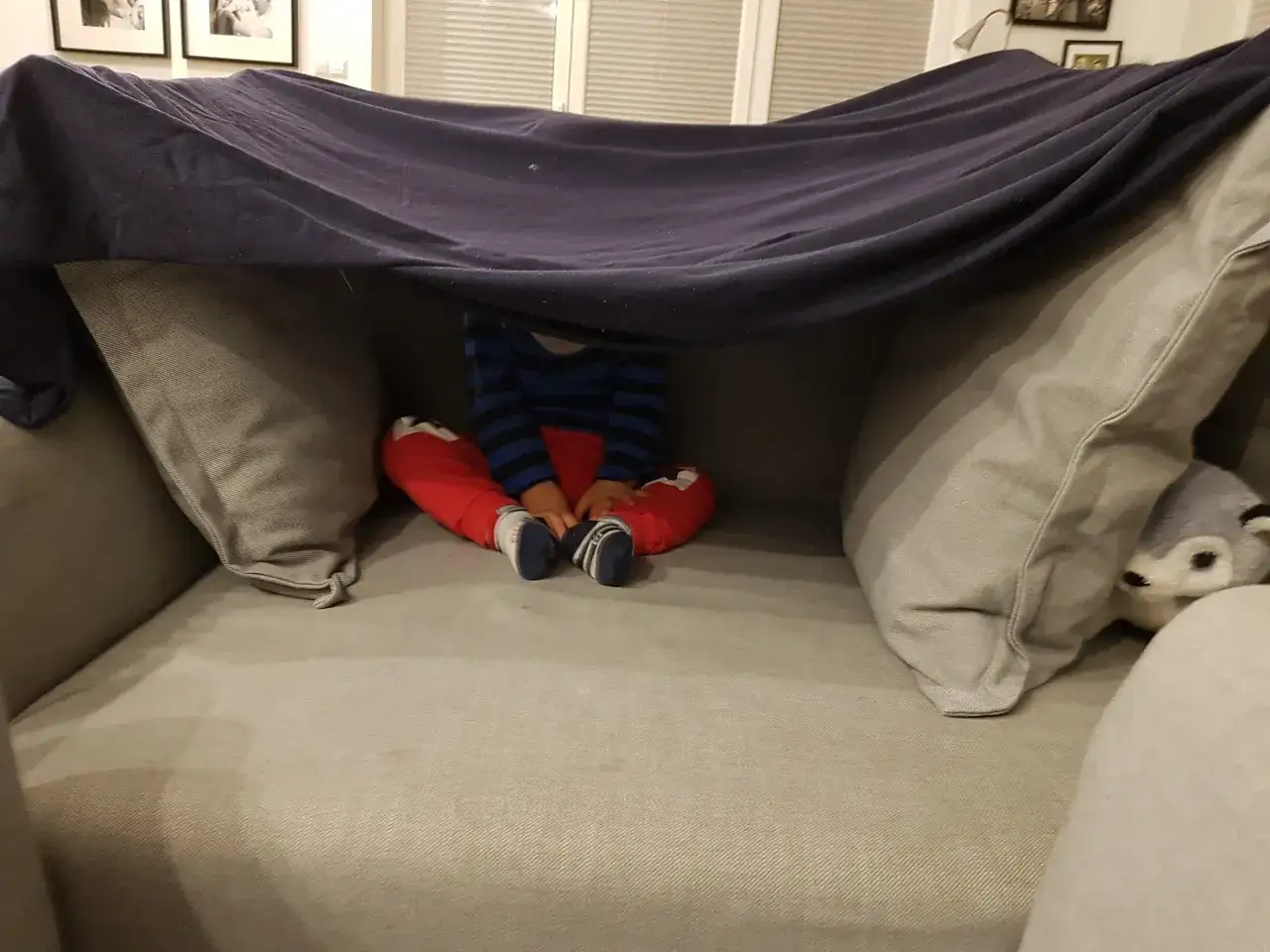 Dziecko siedzi w przytulnej bazie z kocy i poduszek, otoczone pluszowym liskiem.