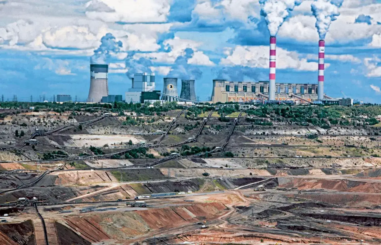 Widok kopalni odkrywkowej i elektrowni z kominami dymiącymi. Pokazuje skalę wydobycia i spalania węgla, sugerując, ile węgla spala elektrownia Bełchatów.