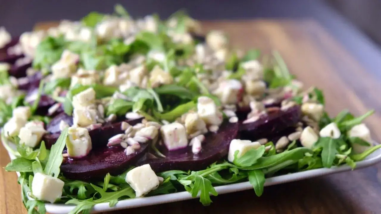Pyszne carpaccio z buraka z fetą, rukolą i pestkami słonecznika na białym talerzu.