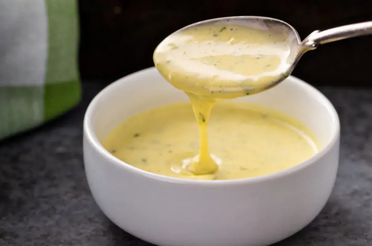 Gęsty, kremowy sos bernenski spływa z łyżki do białej miseczki. Idealny przepis na sos bernenski.