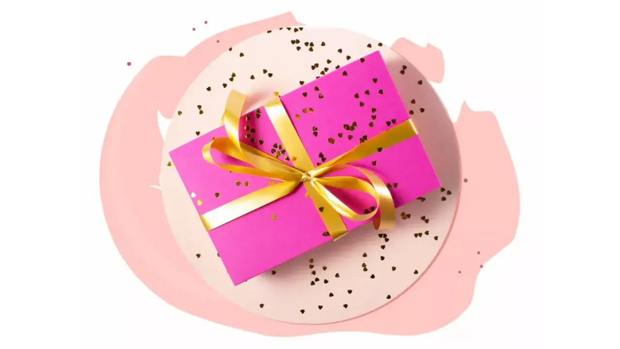 Różowe pudełko z prezentem, ozdobione złotą wstążką i serduszkami. Zastanawiasz się, ile kosztuje impreza urodzinowa na 20 osób?
