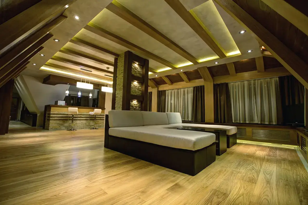 Nowoczesne lampy na poddasze skosy oświetlają przytulne wnętrze z drewnianymi belkami i wygodną kanapą.