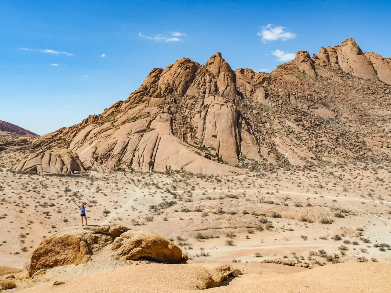 Spitzkoppe Namibia: osoba z radością wita pustynny krajobraz z piaskowcowymi g&oacute;rami w tle.