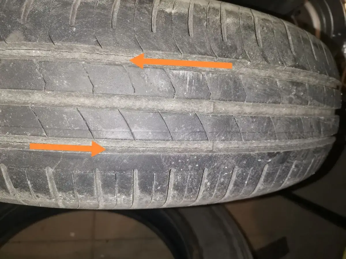Widoczne mikropęknięcia na bieżniku opony, zaznaczone pomarańczowymi strzałkami, świadczą o jej zużyciu.