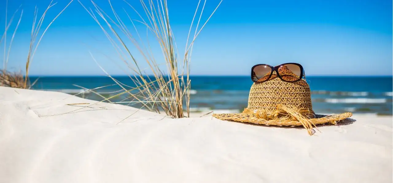 Słomkowy kapelusz z okularami przeciwsłonecznymi na piaszczystej plaży. Idealne miejsce, gdzie na wakacje nad morze.