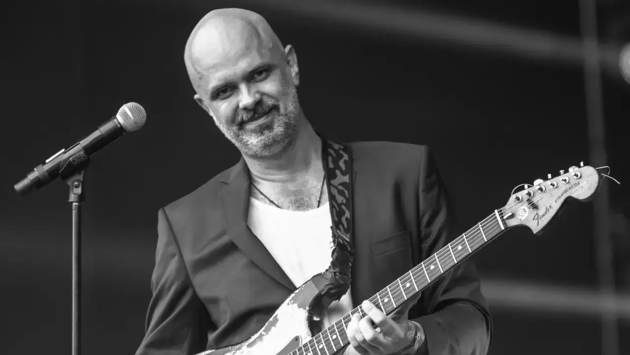 Jacek Budyń Szymkiewicz gra na gitarze Fender Stratocaster, z mikrofonem obok.