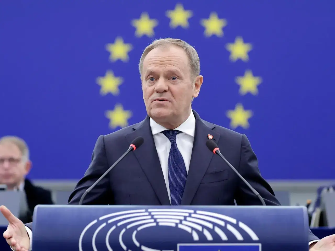 Donald Tusk przemawia na tle flagi UE. Czy Tusk zna angielski? Jego wystąpienie w Parlamencie Europejskim sugeruje, że tak.