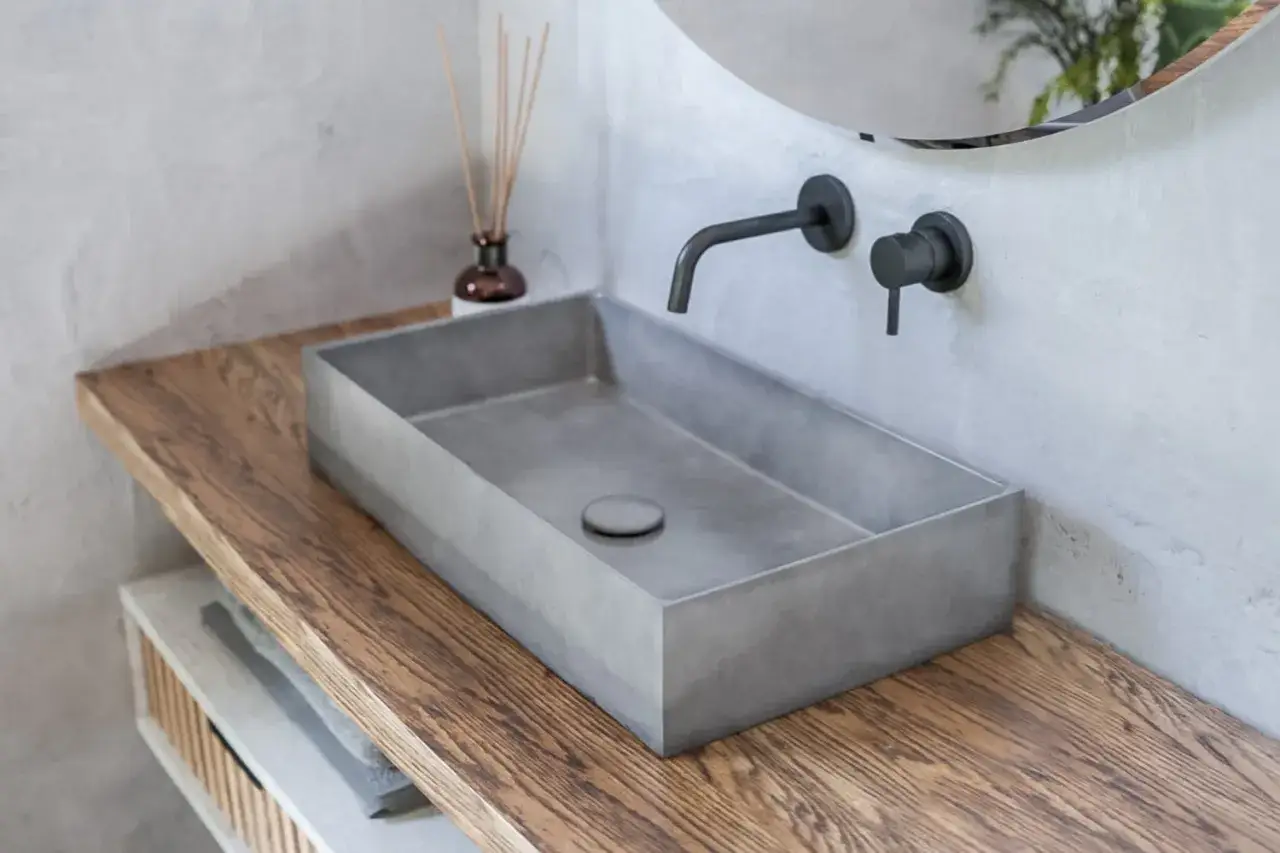 Nowoczesna łazienka z prostokątną umywalką z betonu, drewnianym blatem i czarną armaturą.