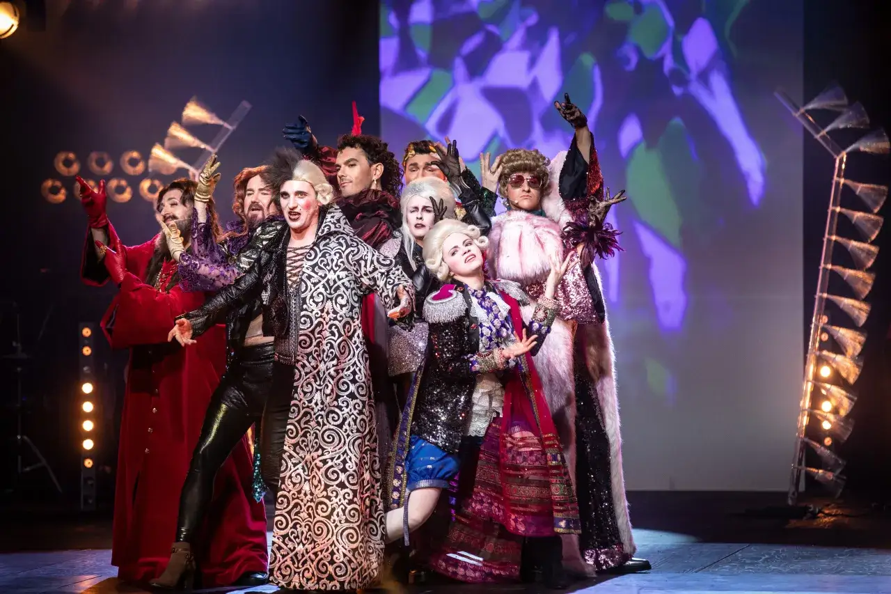 Aktorzy w barwnych strojach na scenie, zapowiadający spektakl z repertuaru teatru muzycznego Warszawa.