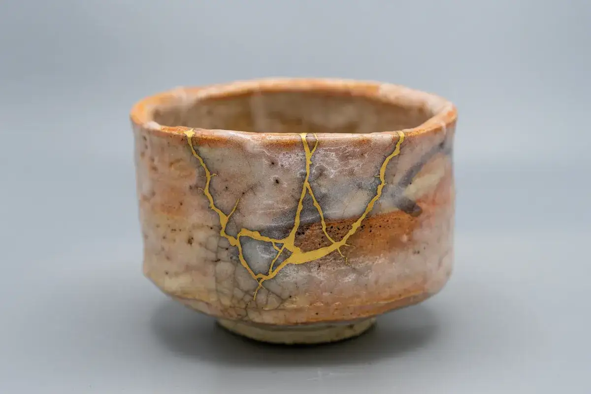 Ceramiczny kubek z widocznymi złotymi pęknięciami, pokazujący, jak naprawić uszczerbiony kubek w stylu kintsugi.