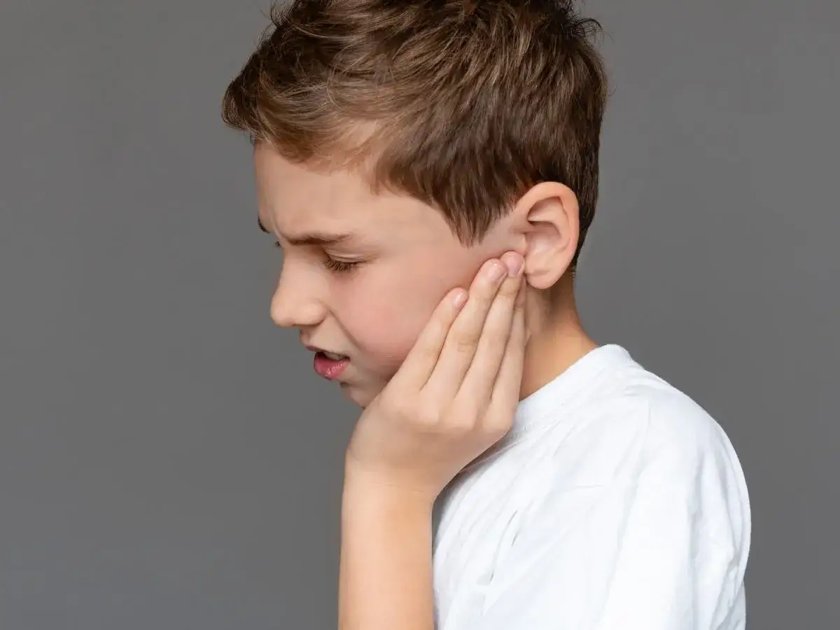 Chłopiec trzyma się za ucho, cierpiąc z powodu bólu policzka od wewnątrz. Jego twarz wykrzywia grymas.
