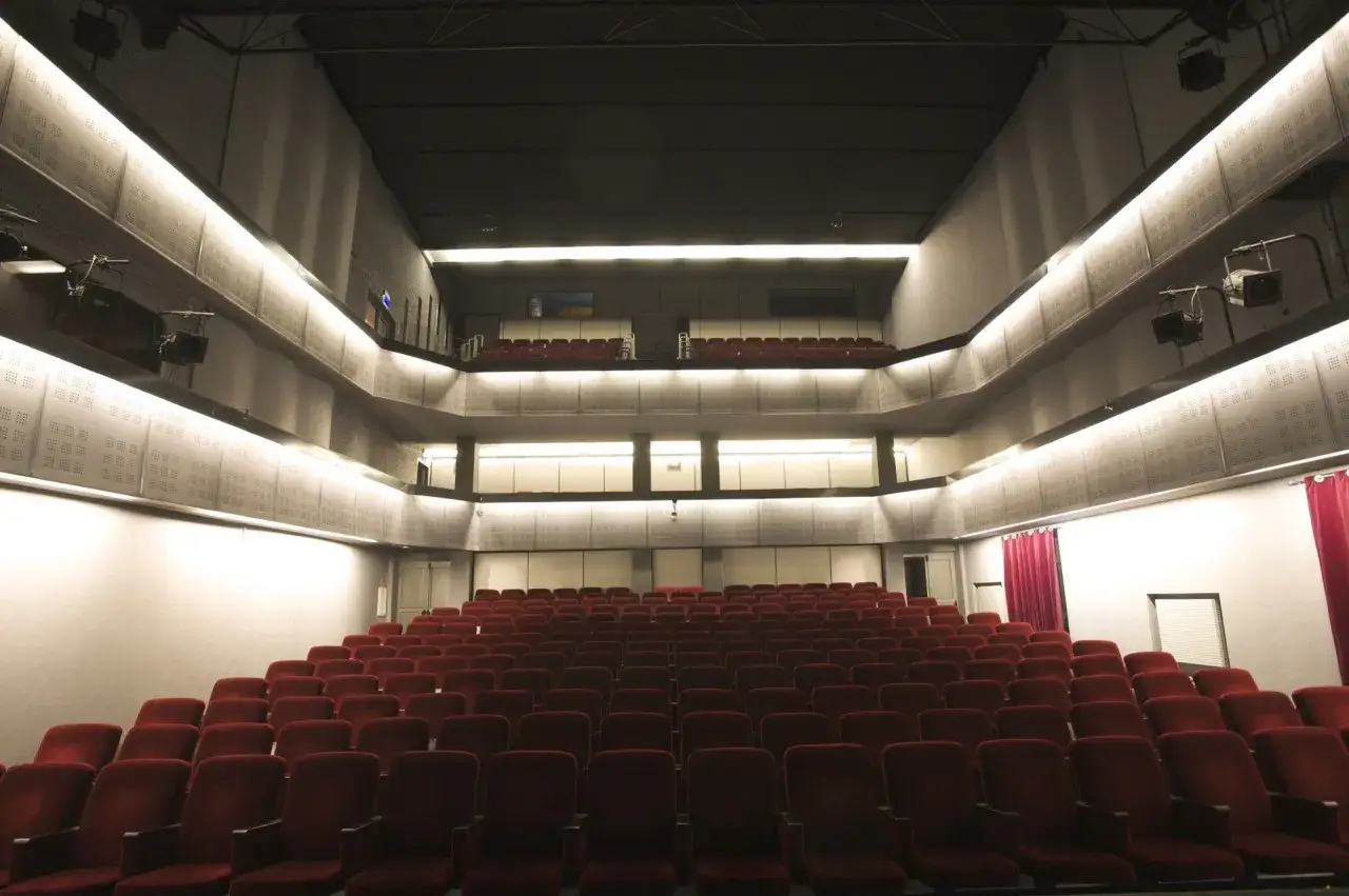 Widok na puste rzędy czerwonych foteli w teatrze Bagatela. Widać piętrową widownię, z lożą lub balkonem na g&oacute;rze.