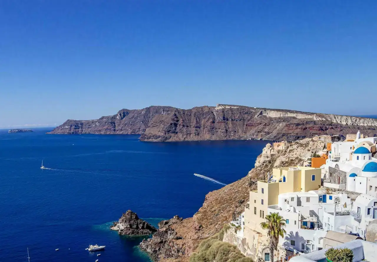 Santorini, Grecja. Białe domy z niebieskimi dachami na klifie, turkusowe morze i skaliste wybrzeże. Idealne miejsce, by zapytać: gdzie do Grecji?