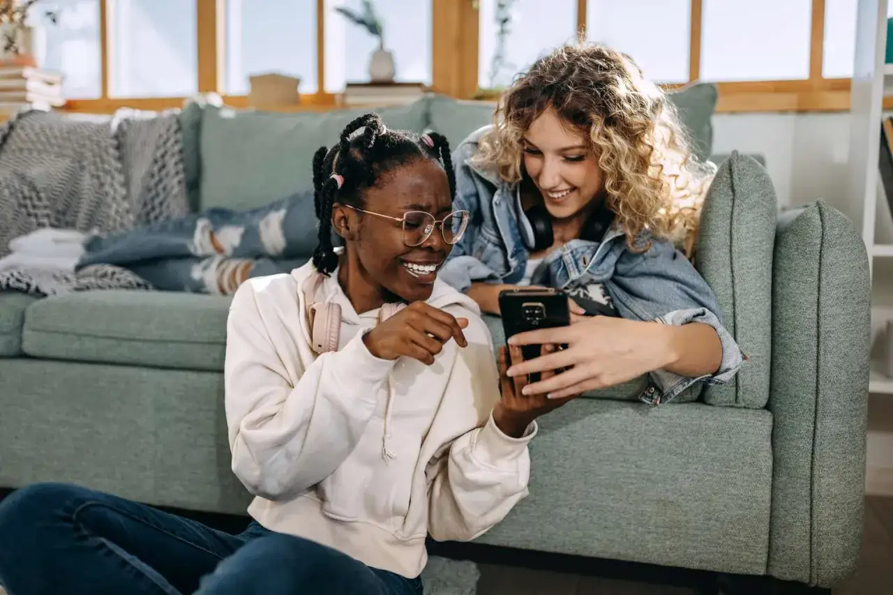 Dwie przyjaci&oacute;łki śmieją się, przeglądając telefon. Może właśnie odkrywają, jak znaleźć kogoś na Tinderze i planują randkę.