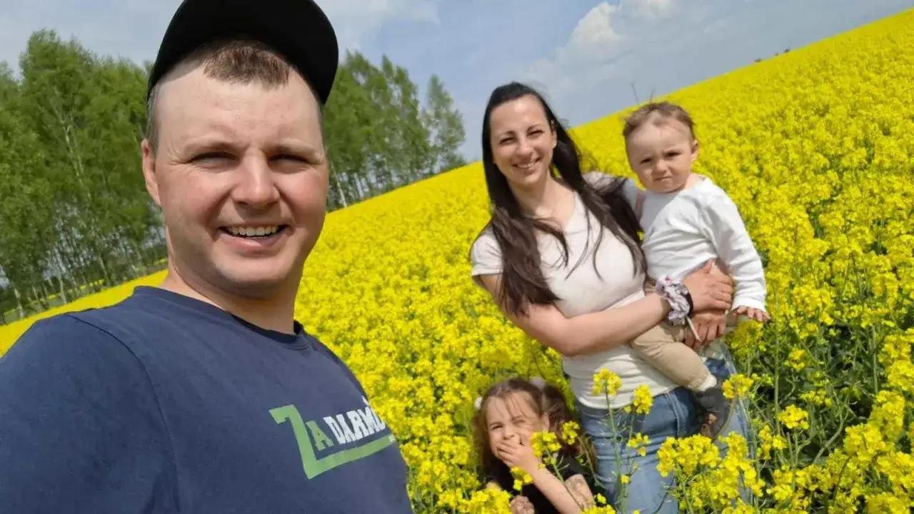 Rodzina na polu rzepaku, gdzie mieszka Jockerfarm. Uśmiechnięty mężczyzna w czapce, kobieta z dzieckiem na ręku i dziewczynka.