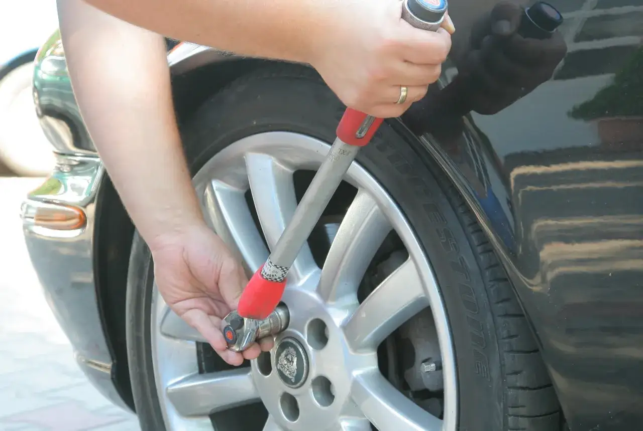 Ręka z kluczem dynamometrycznym dokręca śruby koła. Tabela momentów dokręcania kół jest kluczowa dla bezpieczeństwa.