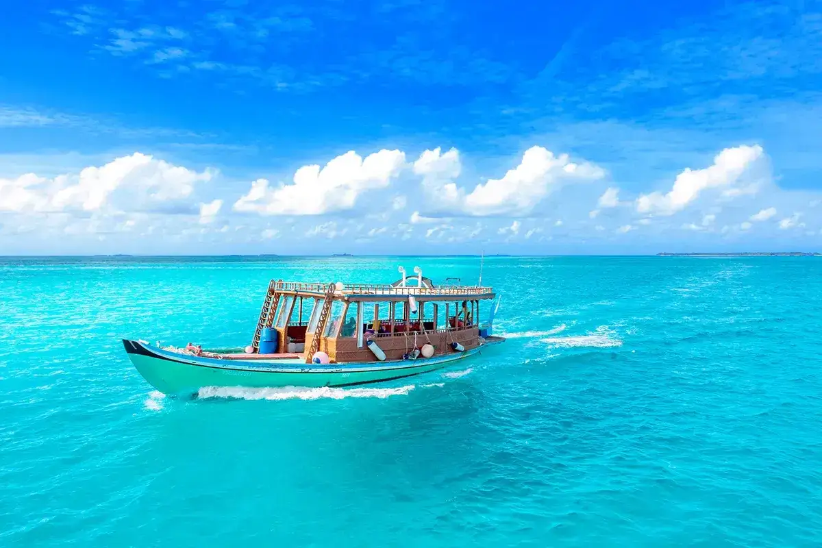 Łódź płynie po turkusowych wodach Malediwów. Nawet gdy jest pora deszczowa na Malediwach, słońce przebija się przez chmury, tworząc rajski widok.