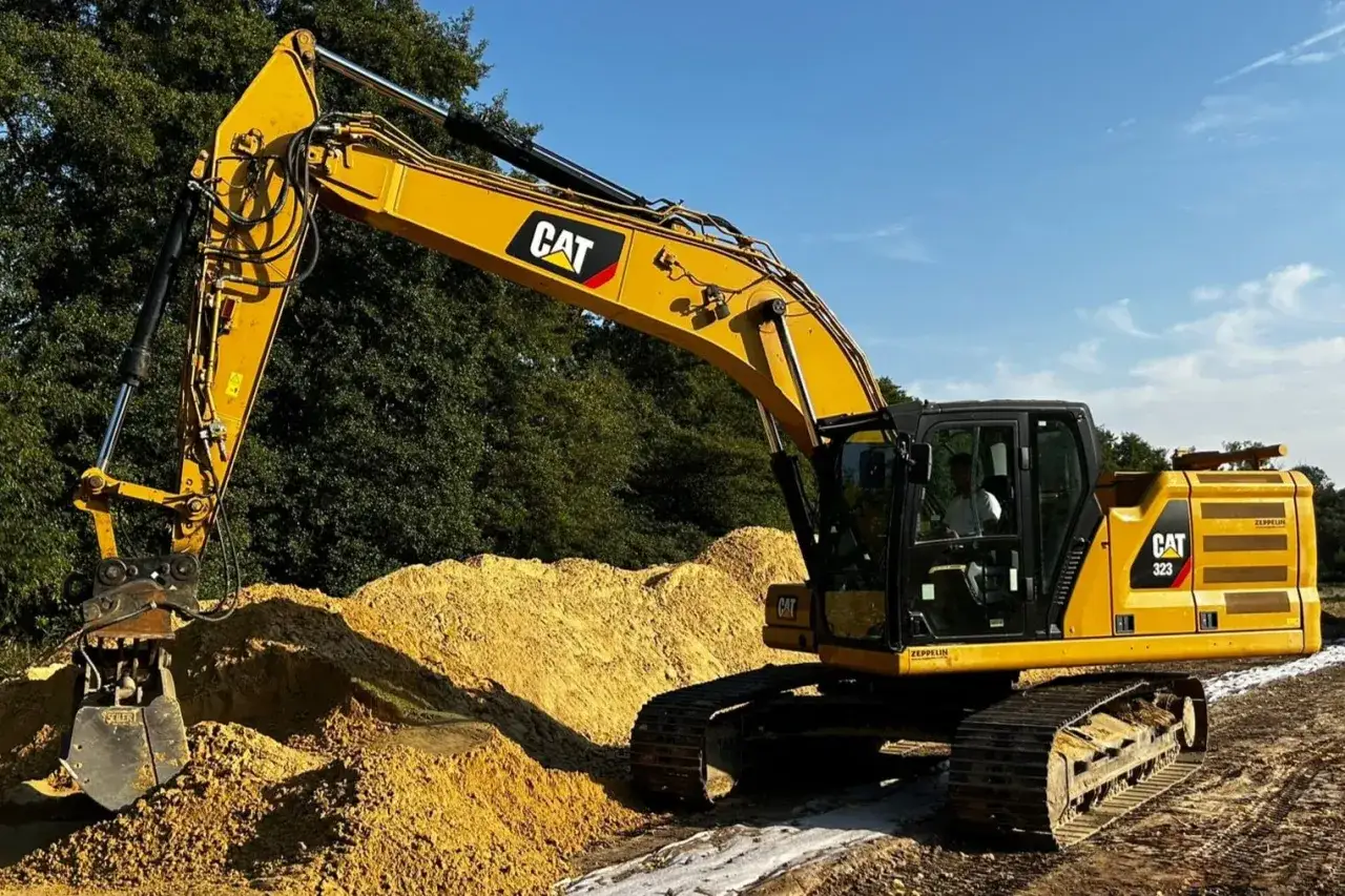 Żółta koparka CAT 323 pracuje na budowie, przesuwając piasek. Zastanawiasz się, ile kosztuje koparka?