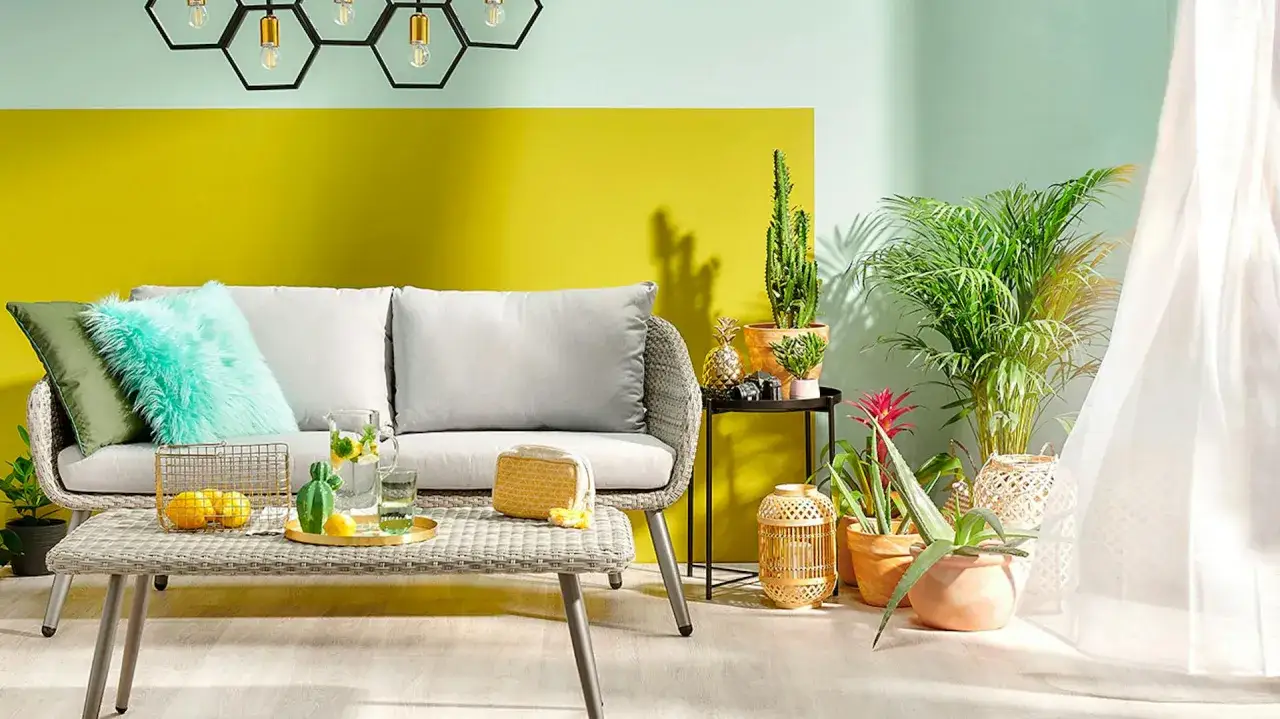 Jasny pok&oacute;j z kanapą i roślinami. Ż&oacute;łta ściana z tyłu to świetny pomysł na pomalowanie pokoju, dodaje energii.