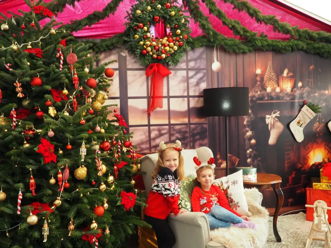 Dwie dziewczynki w świątecznych strojach siedzą obok choinki, tworząc idealną scenę, gdzie pojechać na święta bożego narodzenia w polsce.