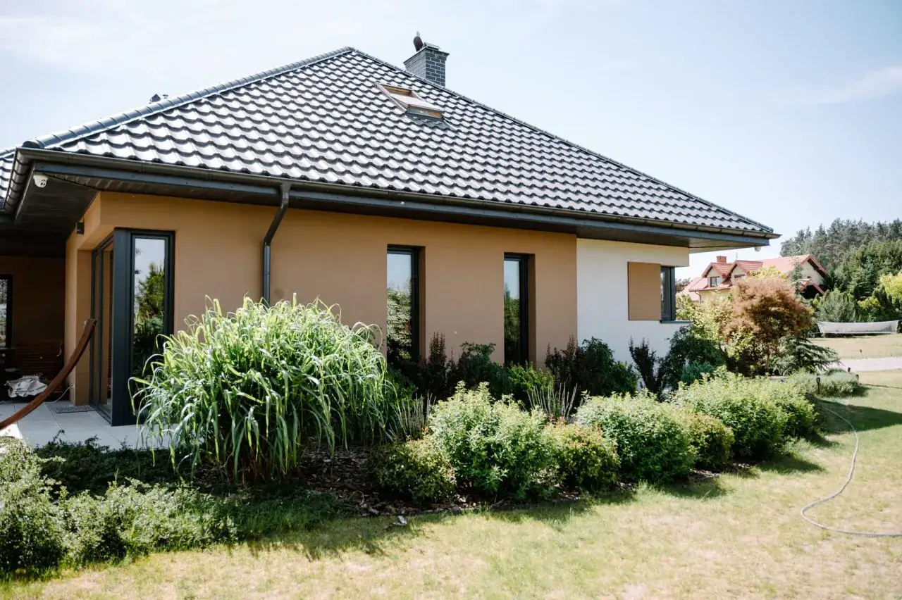 Nowy dom z nowoczesnymi oknami, po udanej wymianie okien, otoczony bujną zielenią.