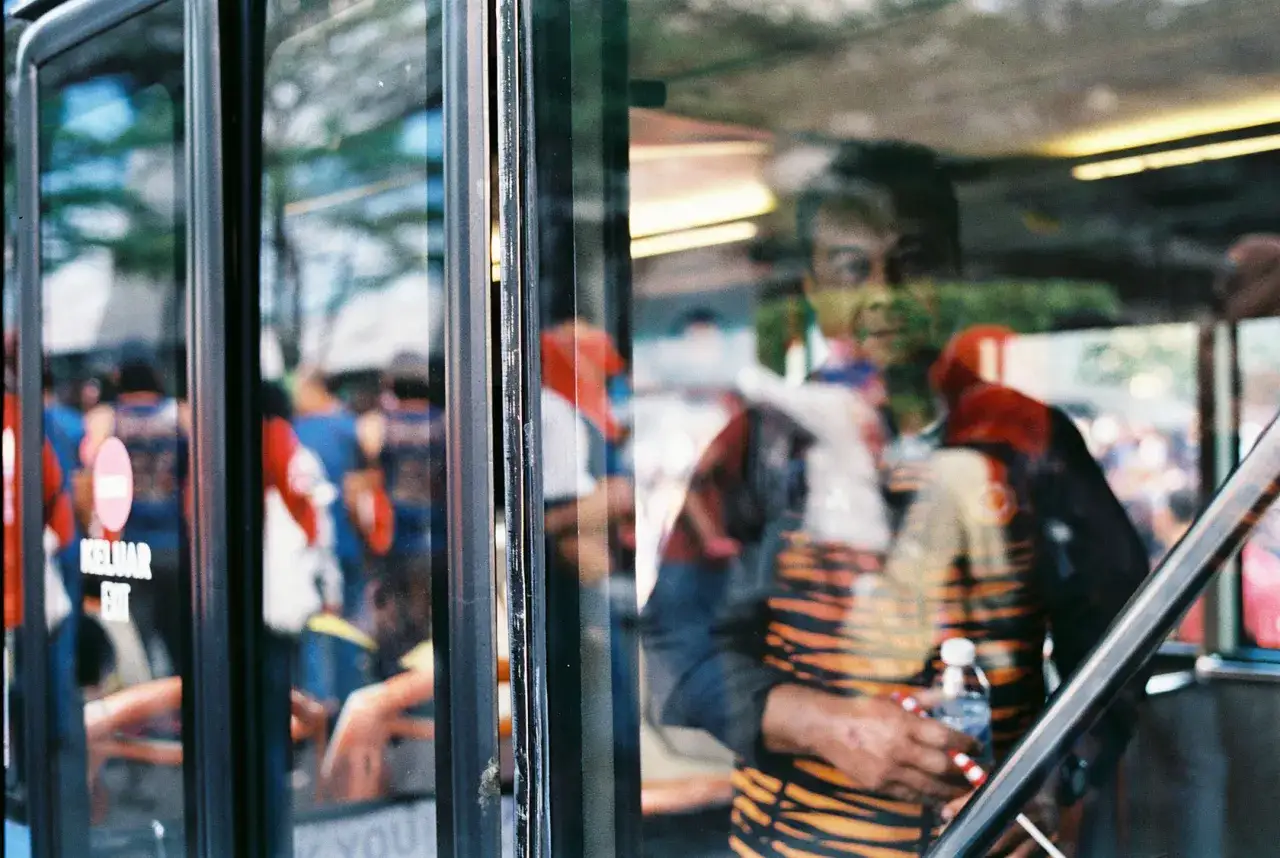 Street photo: odbicie mężczyzny w paski na szybie autobusu, obok pasażerowie.