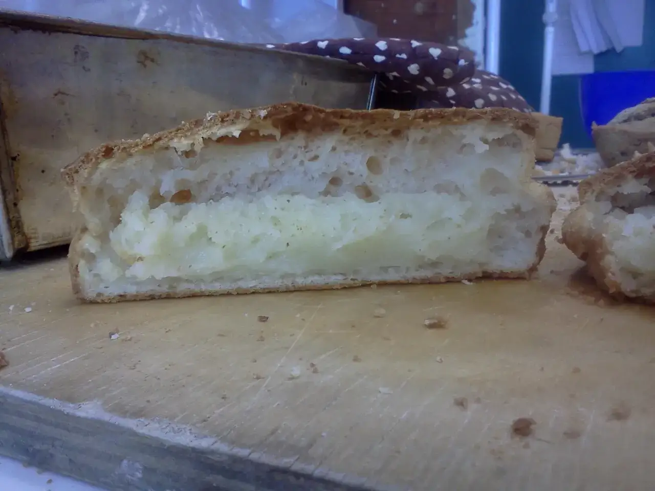 Puszysty chleb bezglutenowy przepis. Pokrojony bochenek z widocznym, jasnym wnętrzem na drewnianej desce.