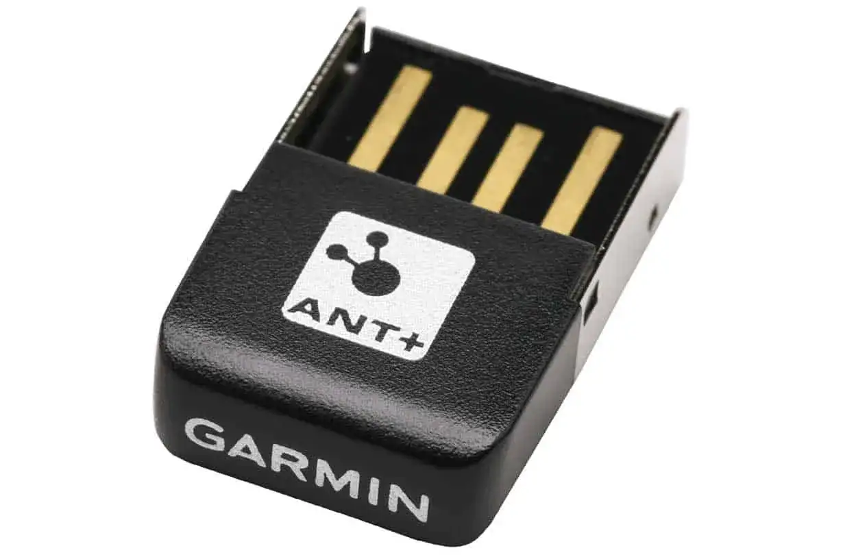 Czarny adapter Garmin z logo ANT+. To małe urządzenie, kt&oacute;re pozwala na bezprzewodową komunikację z innymi urządzeniami sportowymi.