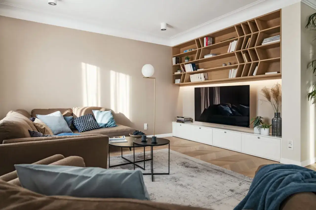 Przytulny salon z sofą i regałem, gdzie dominują kolory pasujące do beżu i brązu, przełamane błękitnymi akcentami.