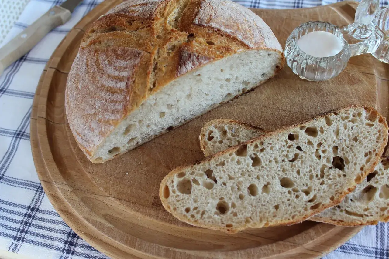 Chleb pszenno żytni na zakwasie, pokrojony na desce, z solniczką i nożem w tle. Idealny na kanapki.