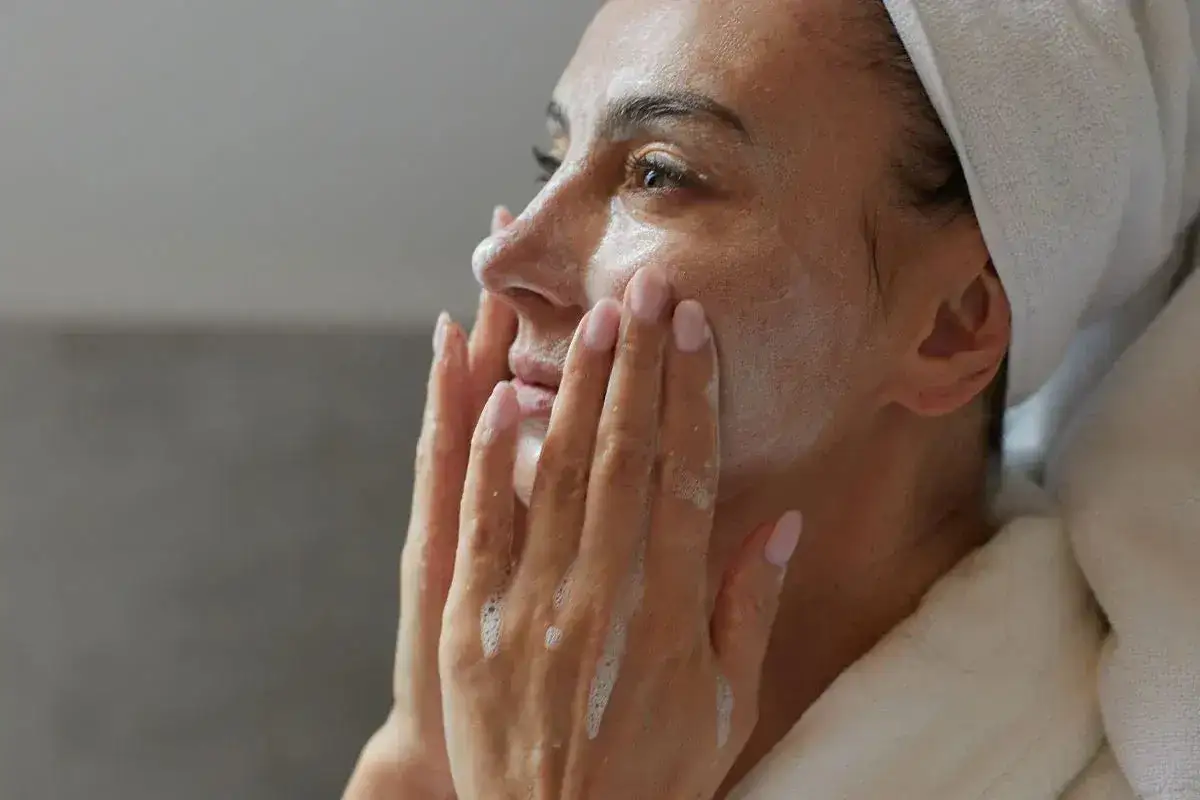 Kobieta z ręcznikiem na głowie delikatnie masuje twarz pianką. To idealny moment, kiedy tonik do twarzy odświeża skórę.