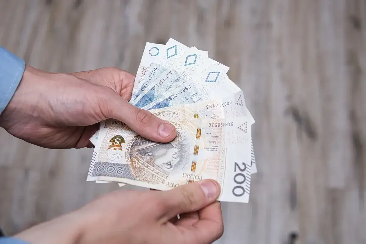 Dłonie trzymają polskie banknoty. Czy to kwota, która odpowiada wysokości renty socjalnej z MOPS?