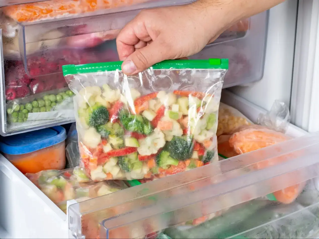 Ręka wkłada do zamrażarki worek z mrożonymi warzywami, pokazując jak mrozić marchew i pietruszkę.