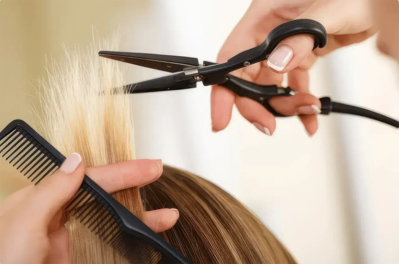 Fryzjerka precyzyjnie ścina pasmo blond włos&oacute;w, używając ostrych nożyczek. Grzebień trzyma włosy gotowe do cięcia.
