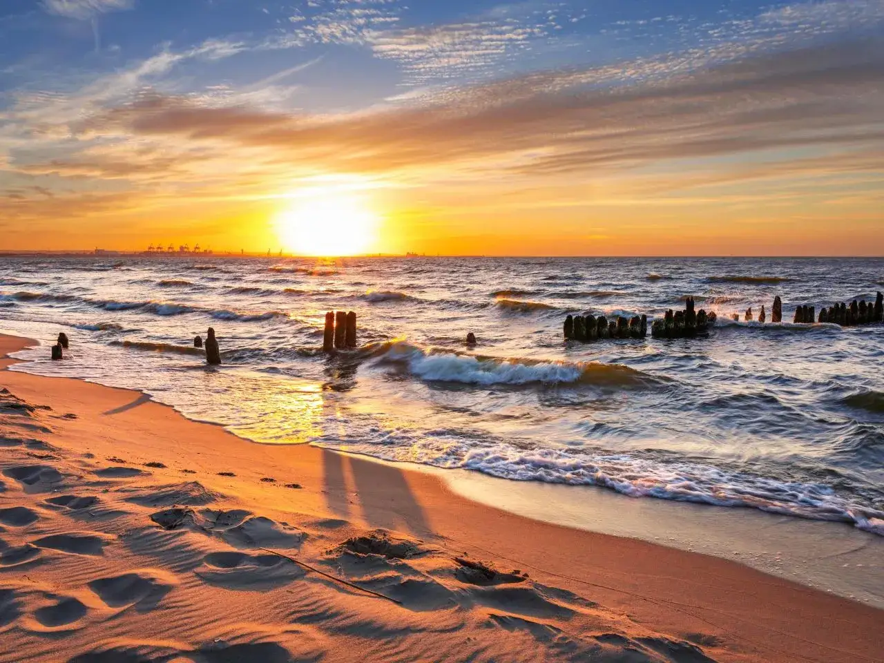 Zachód słońca nad Bałtykiem, idealne miejsce na wakacje w Polsce nad morzem. Piasek, fale i drewniane pale tworzą malowniczy krajobraz.