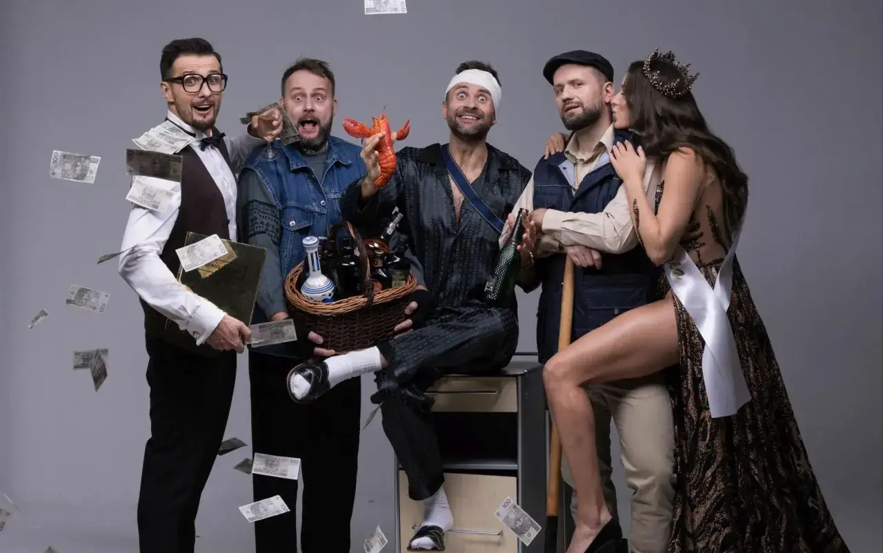 Kabaret z Kielc w szampańskim nastroju. Pieniądze lecą z nieba, a na pierwszym planie krab i kosz pełen alkoholu.