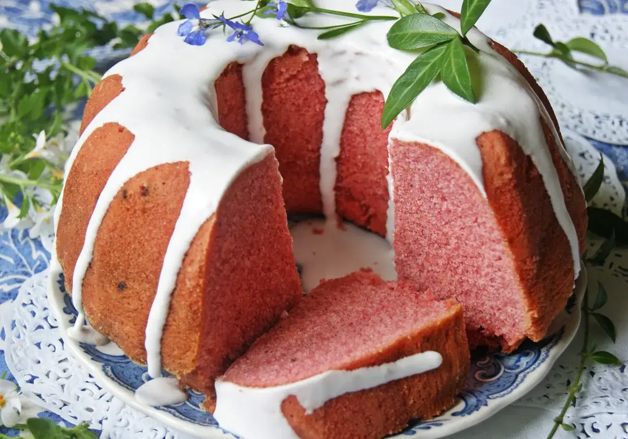 Różowa babka z kisielem, udekorowana lukrem i zielonymi listkami, wygląda apetycznie.