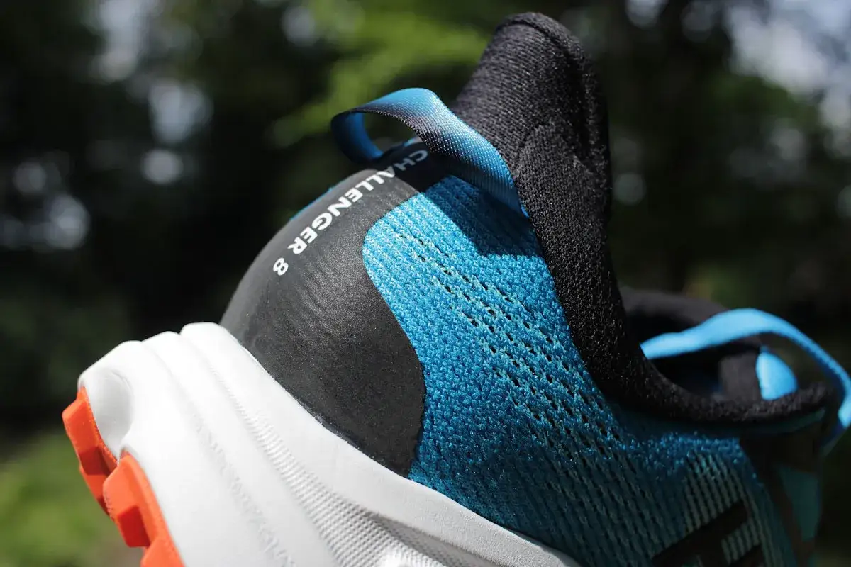 Błękitno-czarny but Hoka Challenger 8 z pomarańczową podeszwą, gotowy na przygodę.